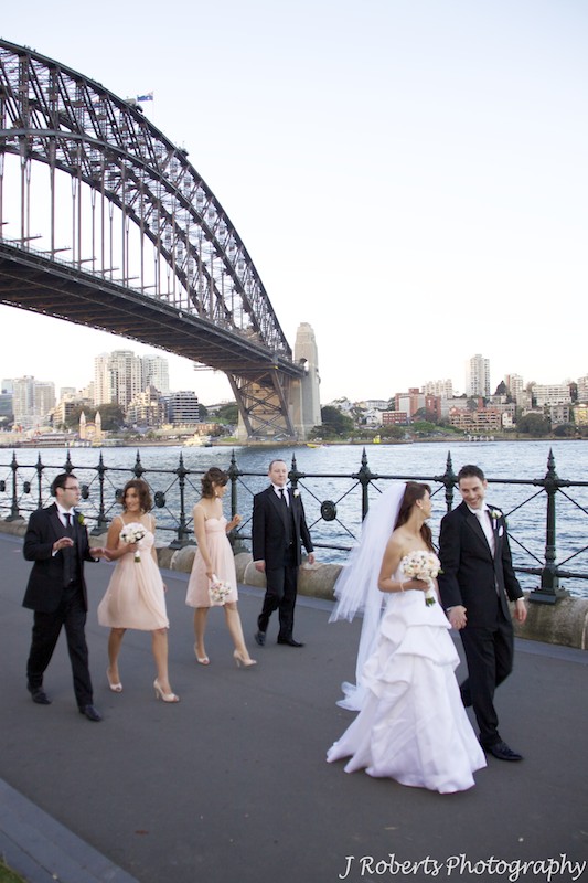 Bridal party walking beside the harbour with Sydney Harbour Bridge behind - wedding photography sydney